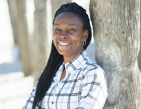 Wounded Warrior Danielle Green leans against a tree at the beach, arms crossed and smiling.
