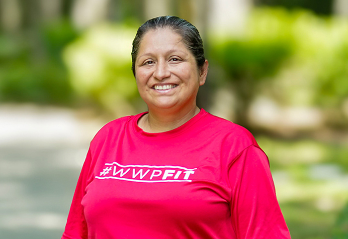 Wounded warrior Maria Edwards stands smiling on a outdoor pathway surrounded by greenery. She is wearing a bright red 