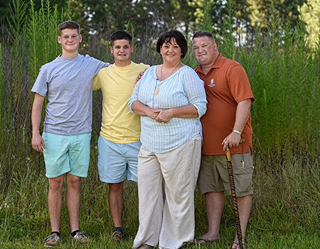 Warrior Tom Marcum stands next to his wife and two sons outside.
