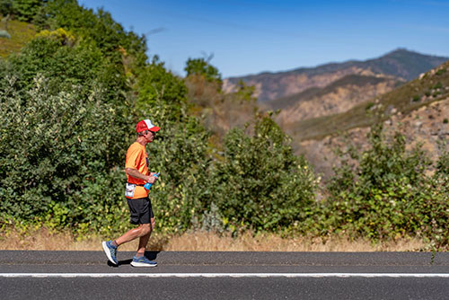 Nels Matson runs on a street in front of mountains during a cross-country trek to support wounded veterans.