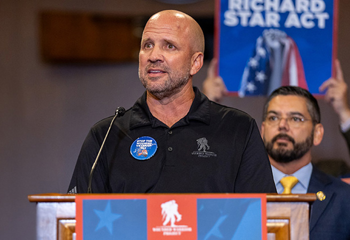 Wounded warrior Dan Nevins stands at a podium and speaks into a microphone during a press conference urging the passing of the Major Richard Star Act.