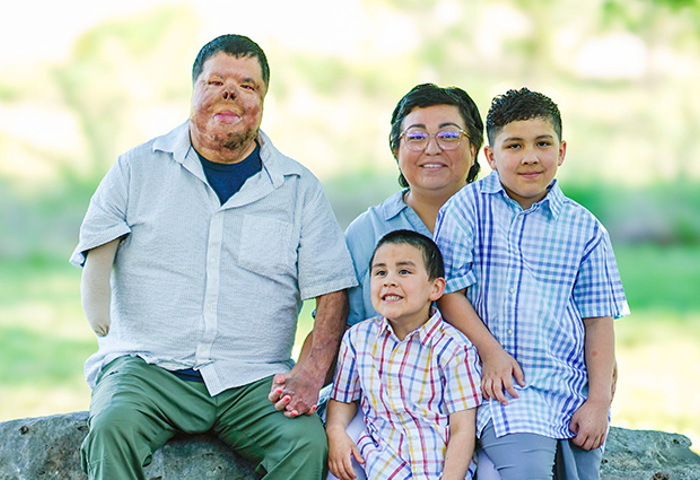 Warrior Anthony Villareal sits with his wife and two sons outside on a large rock under the shade of a tree.