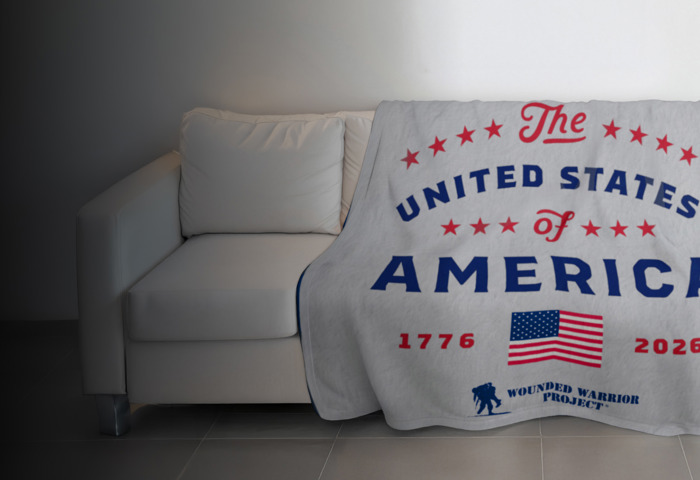 Grey blanket with red & blue font designed to commemorate America’s 250th Anniversary with a WWP logo, draped over a couch.