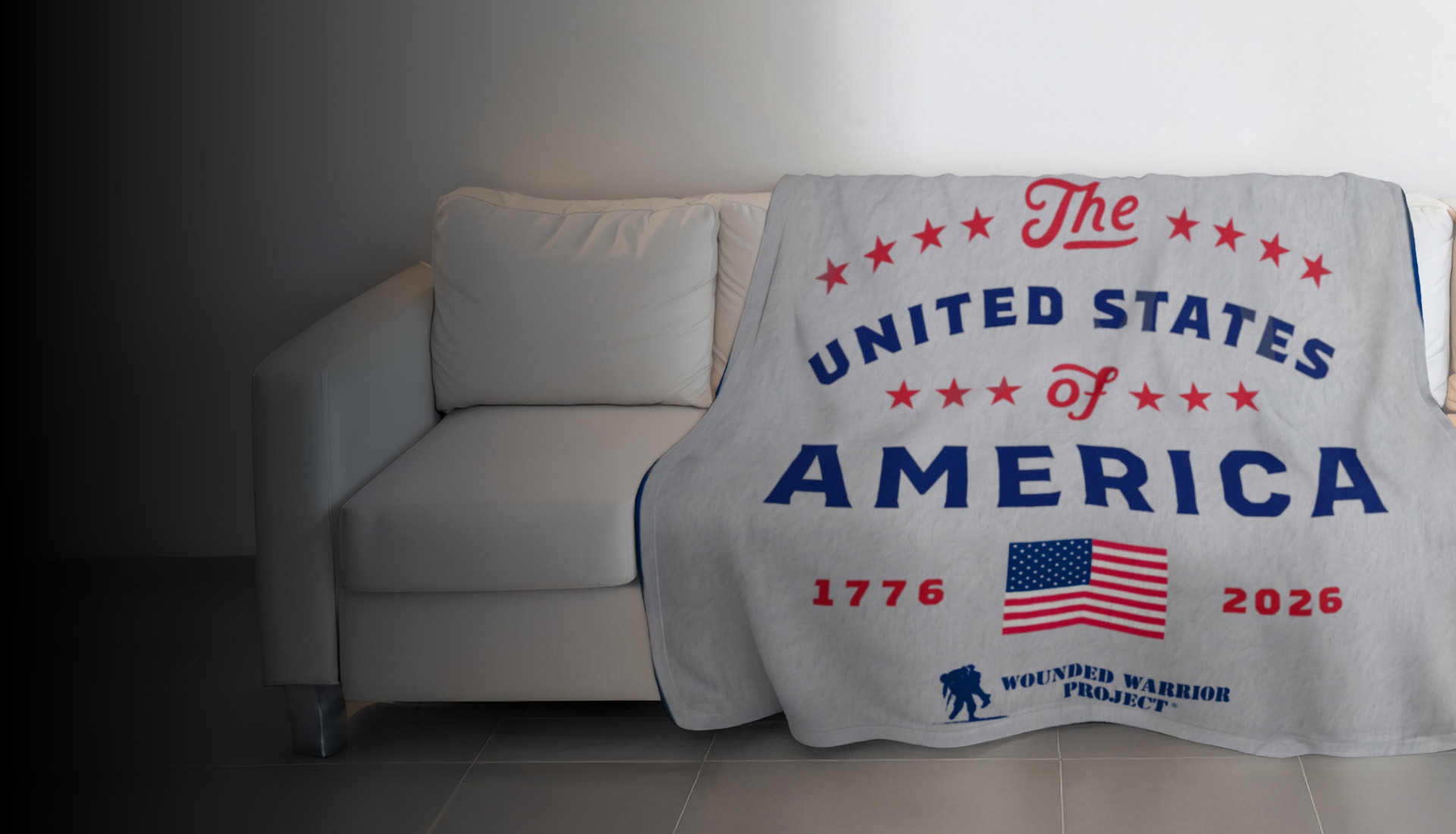 Grey blanket with red & blue font designed to commemorate America’s 250th Anniversary with a WWP logo, draped over a couch.