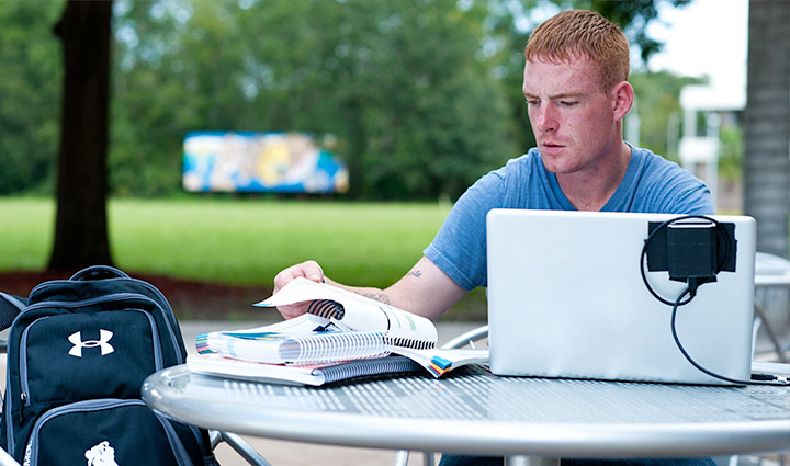 Hombre sentado con una laptop, mirando libros