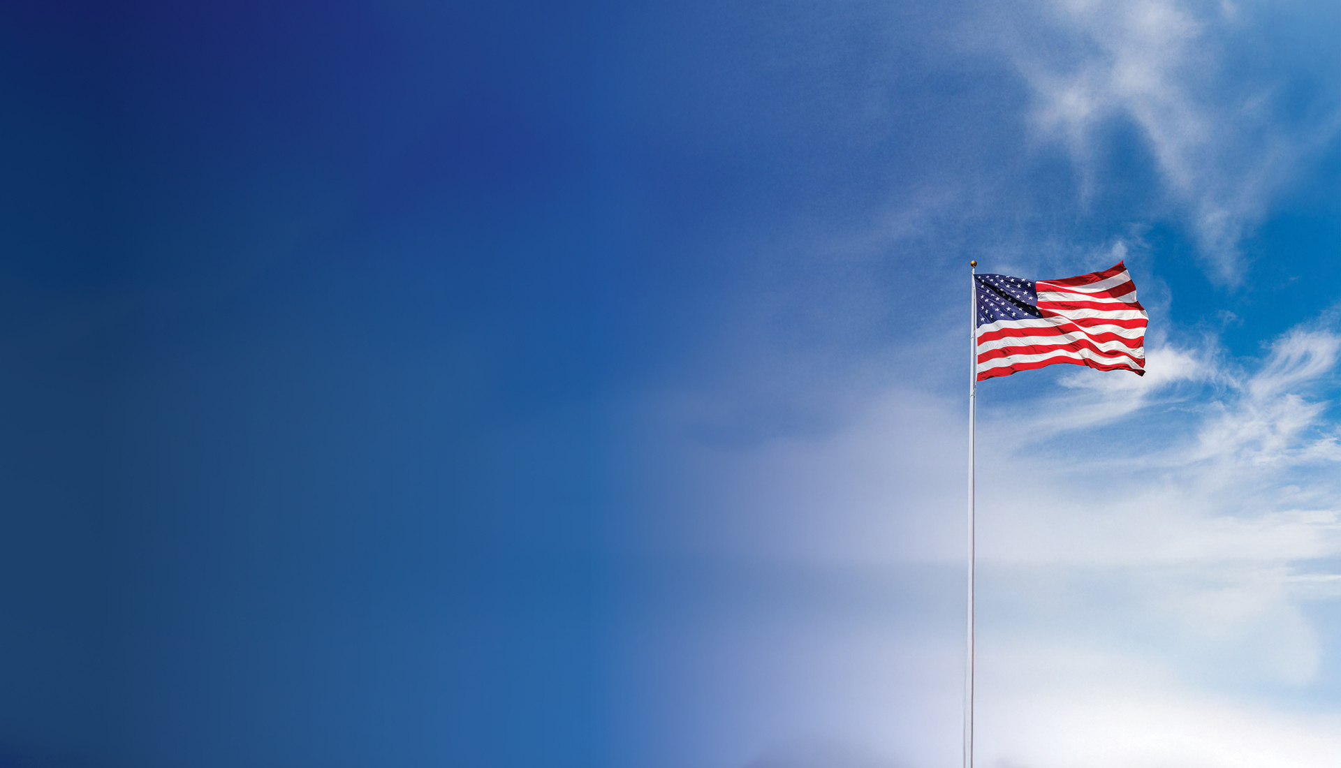 American flag waving on a flagpole against a bright blue sky with wispy clouds on a sunny day.