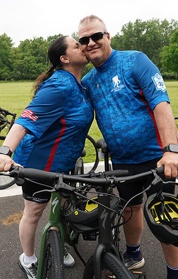 Nora kisses David on the cheek as they each hold their bikes with one hand.