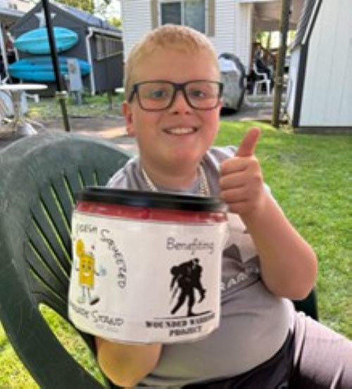 Young boy giving a thumbs up while holding a donation can labeled “Benefiting WWP”