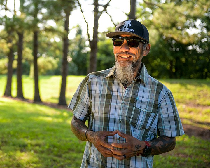 Ray Andalio, veterano herido, parado en un parque, sonriendo y usando gafas de sol y una gorra de WWP.