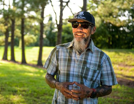 Wounded warrior Ray Andalio standing in a park, smiling and wearing sunglasses and a WWP hat.