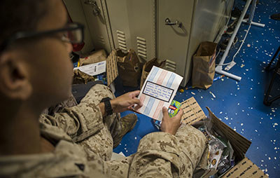 A U.S. Marine opens a care package aboard the amphibious dock landing ship USS Comstock. Photo by Lance Cpl. Gadiel Zaragoza/Provided by DVIDS (The appearance of U.S. Department of Defense (DoD) visual information does not imply or constitute DoD endorsement.)