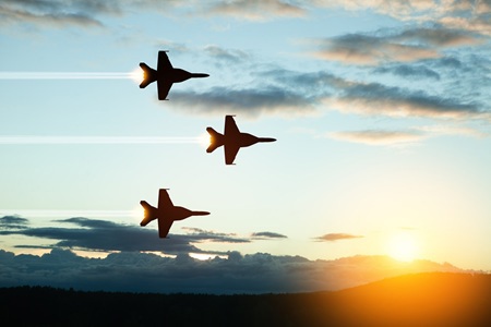 Three military planes flying in formation at sunrise.
