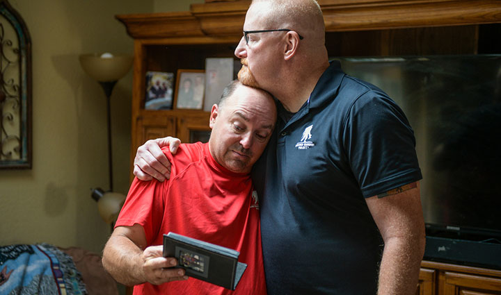 Nick Bennett y Dan Miller de Wounded Warriors se abrazan mientras miran fotos de la familia de Nick.