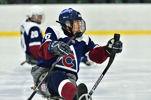 Carla on the ice in a hockey rink wearing sled hockey gear.