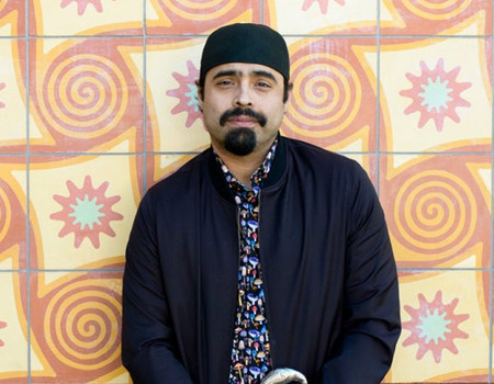 Sal Gonzalez stands smiling in front of a colorful tile wall.