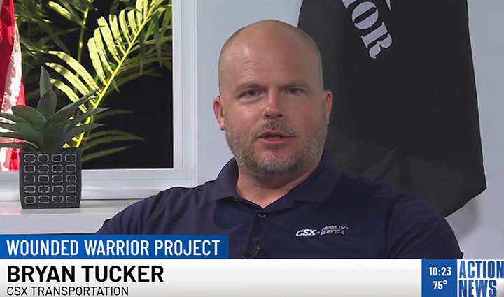 Bryan Tucker from CSX participates in a television interview wearing a golf shirt with a WWP flag in the background.