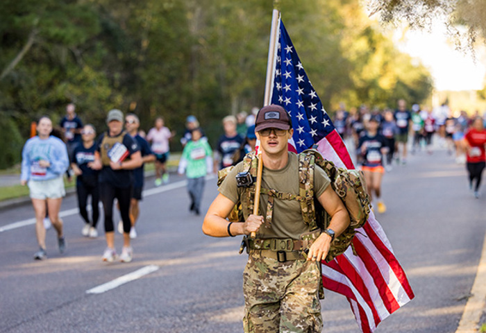 Carry Forward participant walking with an American flag with fellow participants on the route behind him.