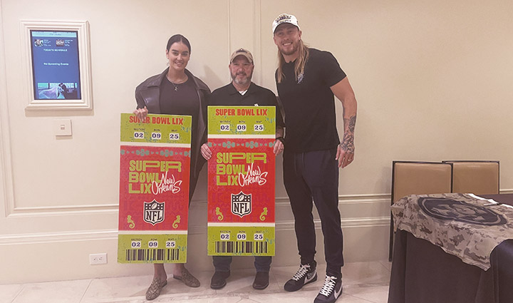 Claire Kittle and wounded warrior Deron Santiny stand holding Super Bowl ticket enlargements next to NFL player George Kittle.