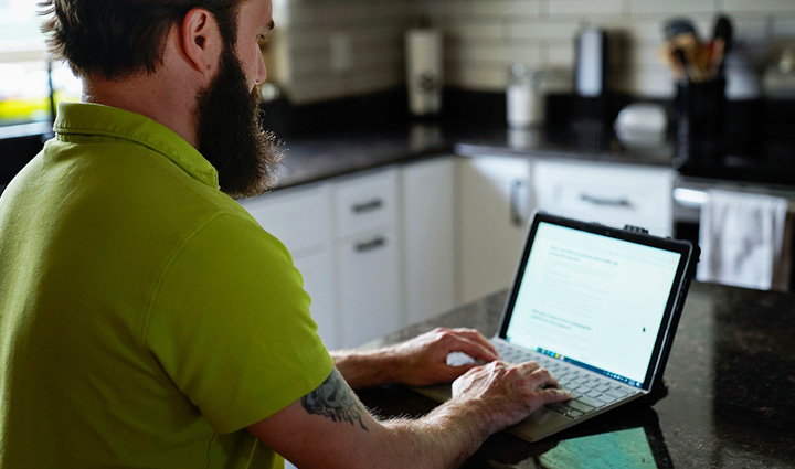 Warrior Drew Carpenter wears a green shirt while working on his computer, sitting at a counter.