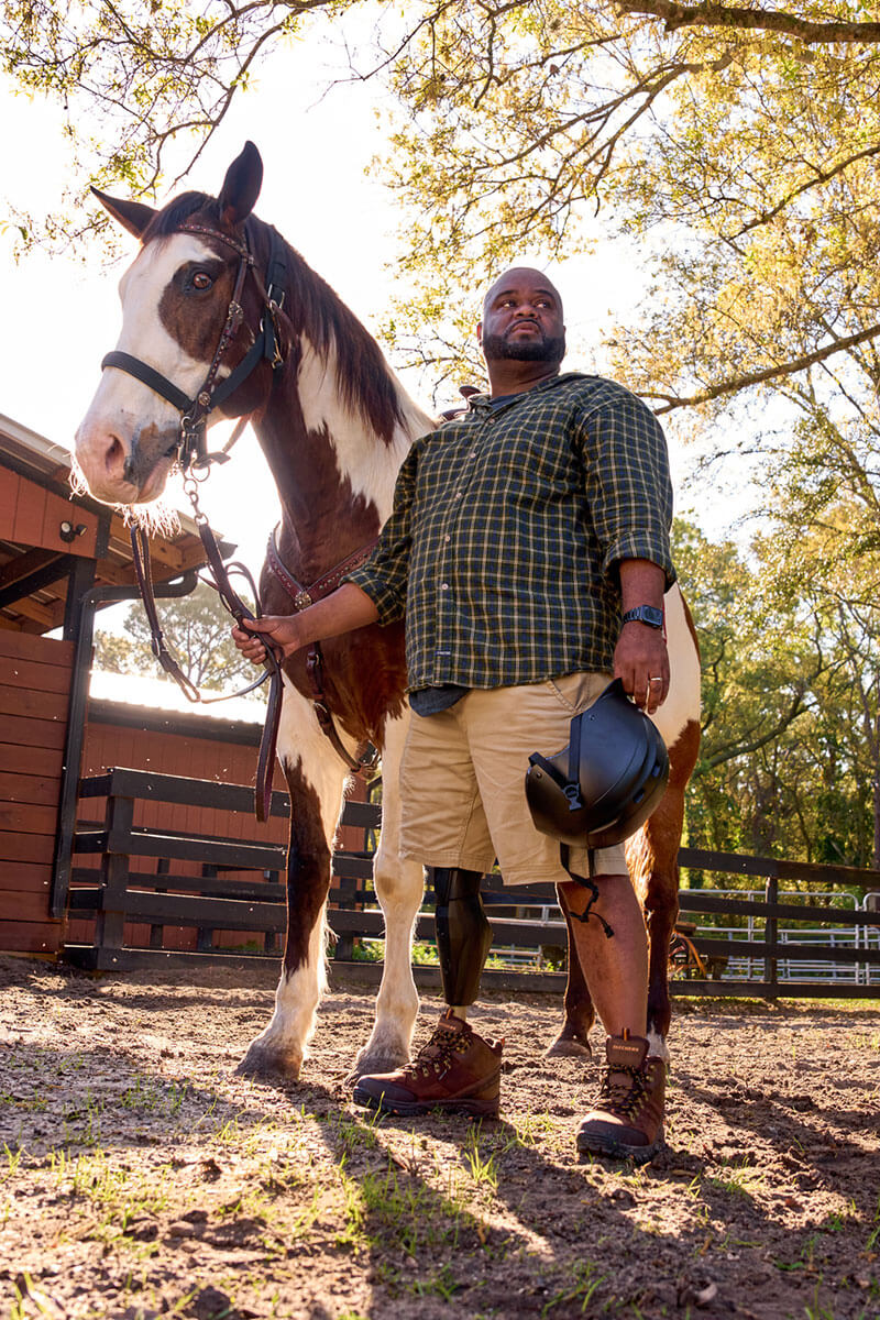 Wounded warrior Chris Gordon standing in an equestrian facility holding a horse by its reins.