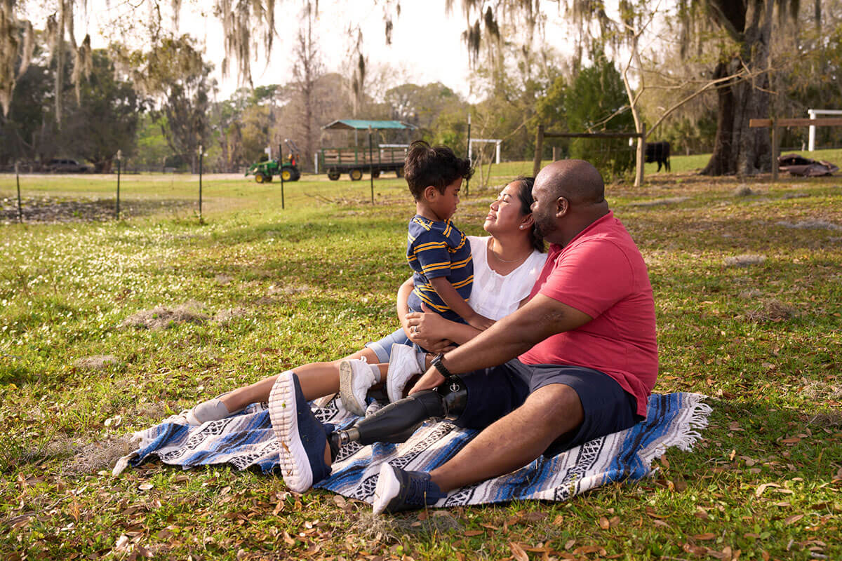 Wounded warrior Chris Gordon, his wife, and son are sitting on a blanket in a field.