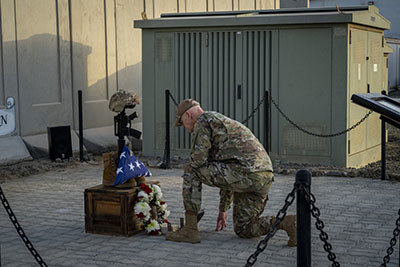 A service member kneels at a Battlefield Cross.