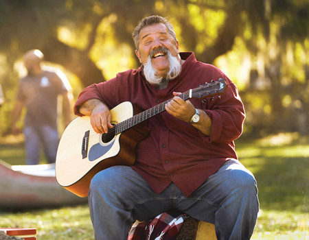 Wounded warrior Aaron Cornelius playing the guitar around a fire during an outdoor event.