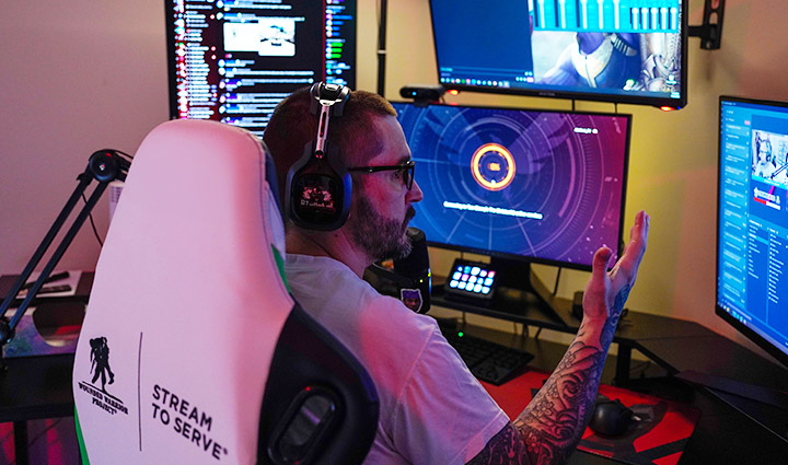 Wounded warrior Xander Hernandez sits in front of multiple monitors speaking into a mic as he streams live to his audience. 