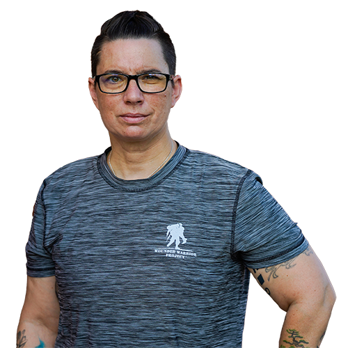 Warrior Beth King stands with her left arm on her hip. She is wearing a heathered gray Wounded Warrior Project T-shirt and black rimmed glasses.