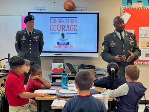 Two Army service members talk to elementary school students.