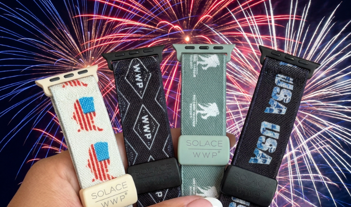 Part of hand showing with French manicure holding four watch bands with American flag, WWP inside diamond, WWP logo, and USA.