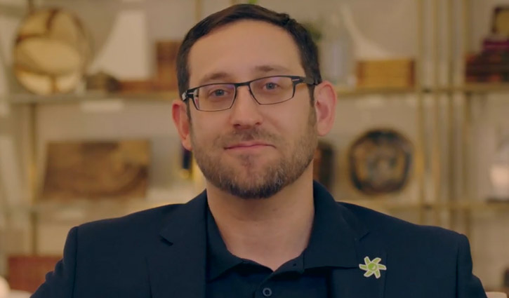 Un hombre de pelo oscuro con una chaqueta azul se sienta a hacer una entrevista cerca de una cámara que no está a la vista.