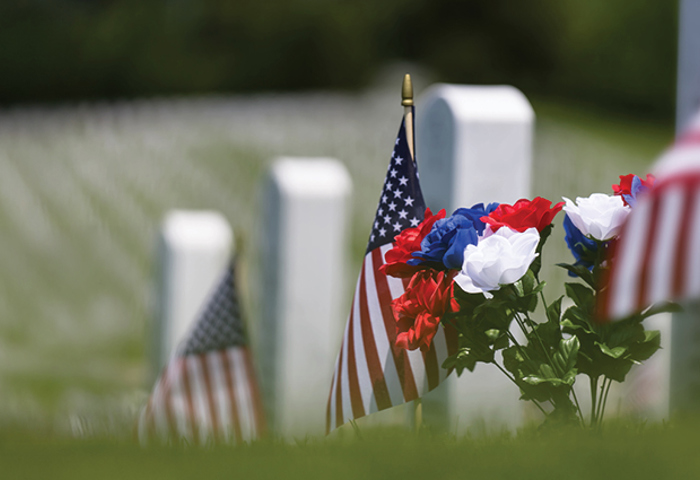 A Memorial Day picture of US flags and flowers by a gravestone at a military cemetery.