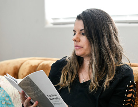 Warrior Melissa McMahon reviewing a benefits brochure while sitting on her couch.