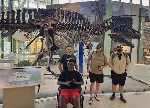 Warriors and Headway San Antonio members pose with a dinosaur fossil at a Texas museum.