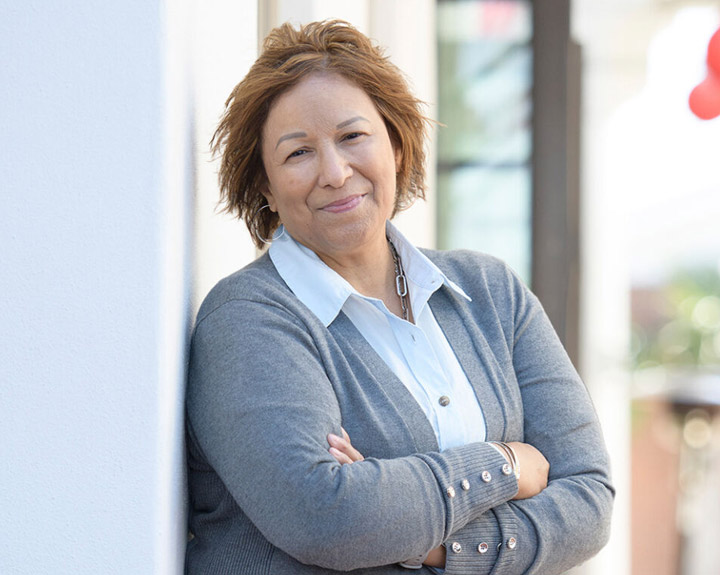 La cuidadora Cindy Parsons posa apoyada contra una pared mientras sonríe y cruza sus brazos.