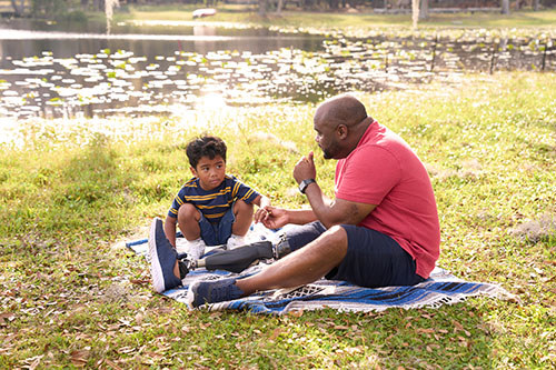 A veteran talks to his young son sitting in a field in front of a lake.