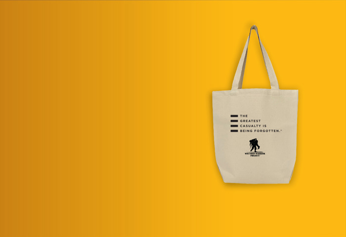 A tan canvas tote bag with the WWP logo and tagline “The Greatest Casualty is Being Forgotten” in black text.