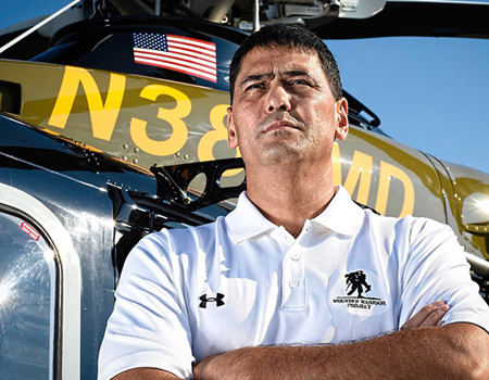 Wounded warrior Claude Boushey stands in front of a helicopter with his arms crossed.