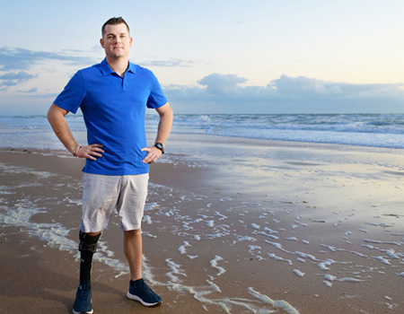 Wounded warrior Mike Larson stands on a sunset beach, proudly showcasing his prosthetic leg with confidence and pride.