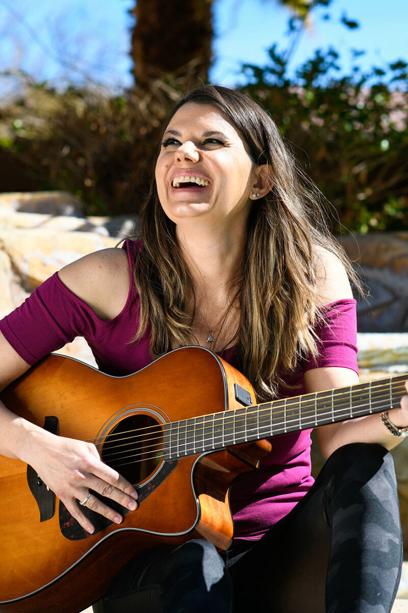 Wounded warrior Melissa McMahon laughing while playing the guitar.