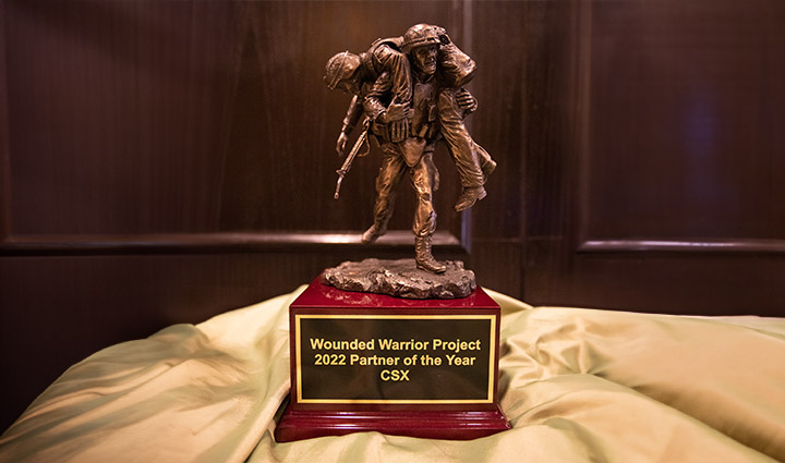 The Corporate Partner of the Year trophy includes a sculpture of one soldier carrying another placed on a wood base with a plaque on the front of it.