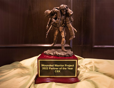 The Corporate Partner of the Year trophy includes a sculpture of one soldier carrying another placed on a wood base with a plaque on the front of it.