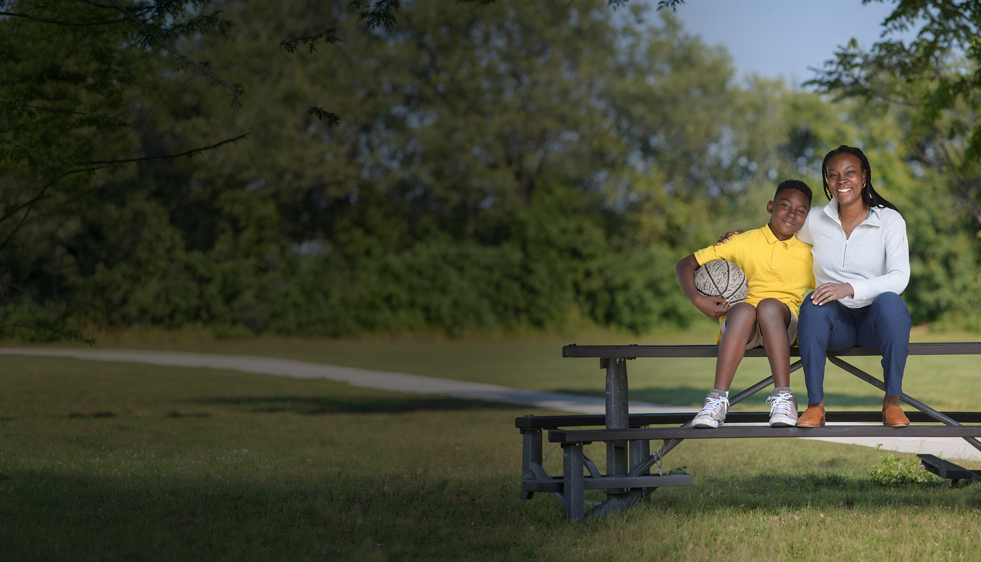 Warrior, Danielle Green sitting in a park with her son holding a basketball with her prosthetic hand.