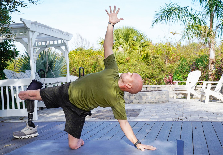 Wounded warrior Dan Nevins practicing yoga in his backyard surrounded by lush foliage.