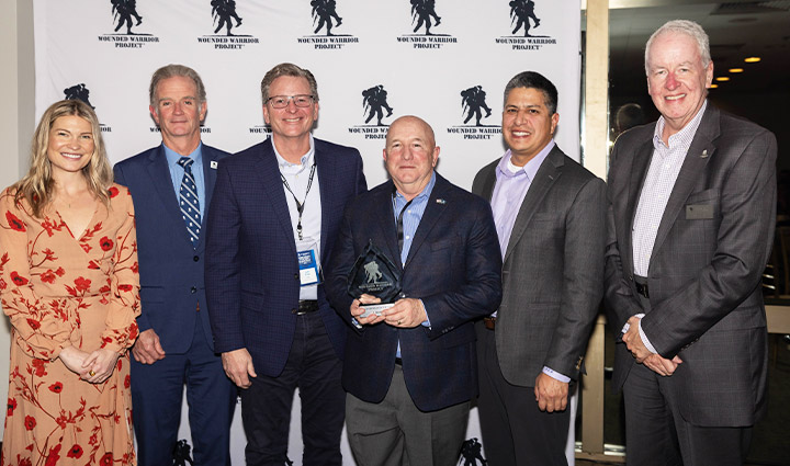 Directivos de WWP y USAA vestidos con ropa formal sonríen de pie delante de un cartel de WWP; uno de ellos sostiene un premio