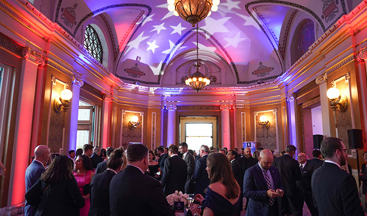 Guests in formal attire mingle in a ballroom lit in red, white and blue during the WWP Courage Awards and Benefit Dinner.