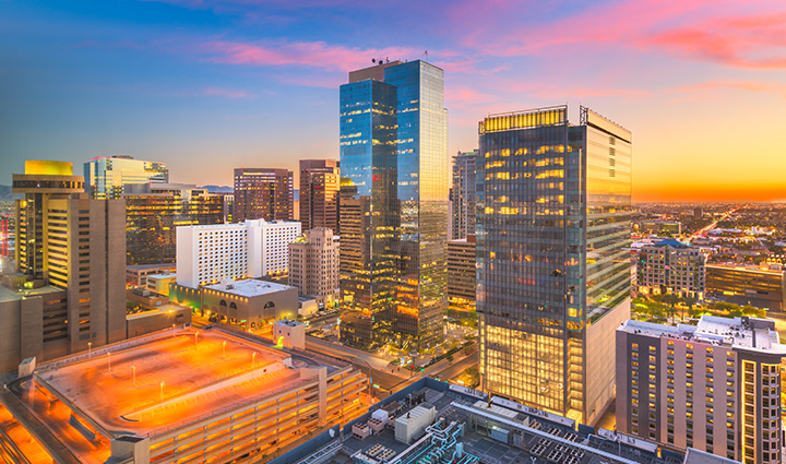 Cityscape of downtown Phoenix at sunset with high-rises, colorful sky, and a lit parking structure in the foreground.